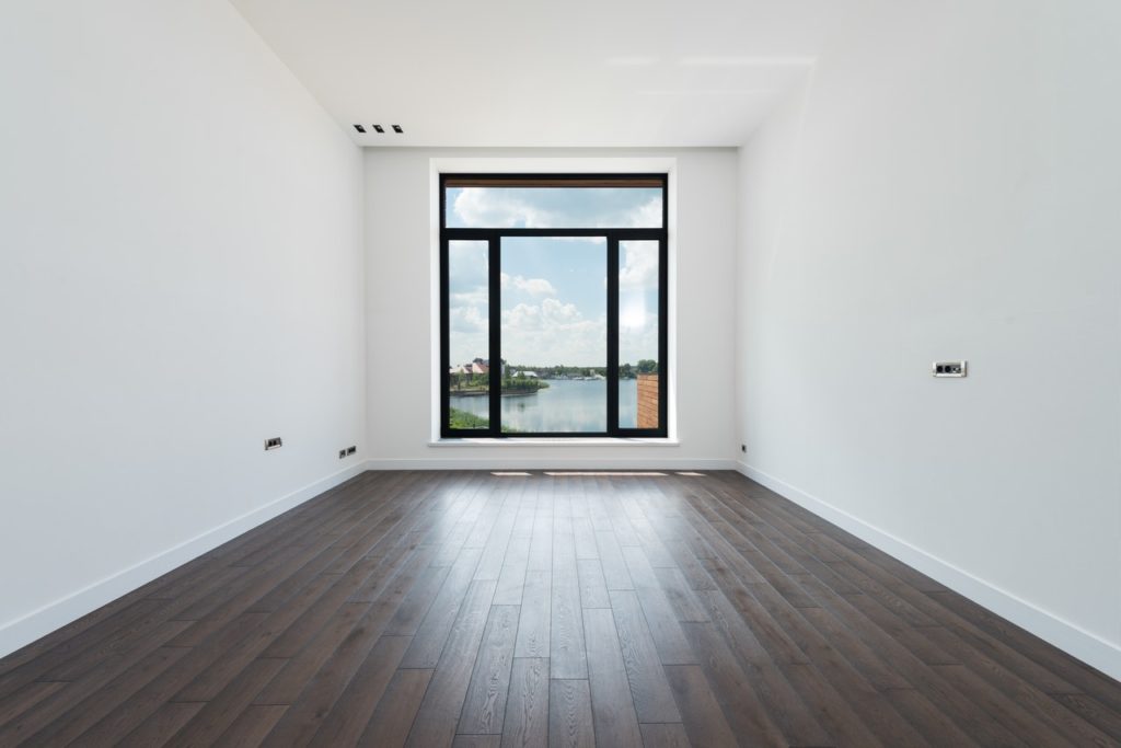 A room with hardwood floor, no furniture and a large window which makes for a cozy minimalist home. 